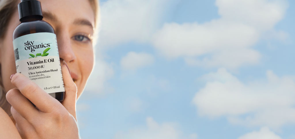 Blond Girl with blue eyes holding a Sky Organics Vitamin E Oil, with a blue sky background
