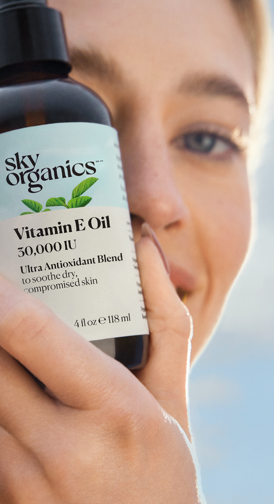 Blond girl with blue eyes holding a Sky Organics Vitamin E Oil bottle. Experience simple personal care with nature's purest and most potent botanics